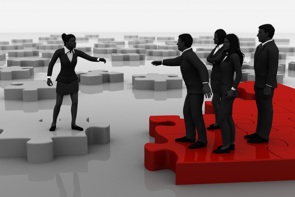 Silhouetted people reaching for each other while standing on jigsaw pieces